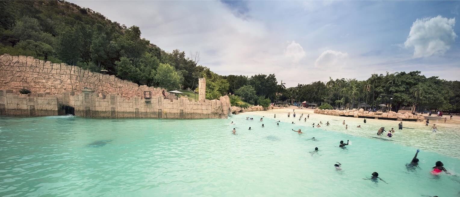 Un groupe de nageurs profite des eaux claires de la piscine à vagues du The Palace of the Lost City, à Johannesburg, sous un ciel ensoleillé et lumineux.