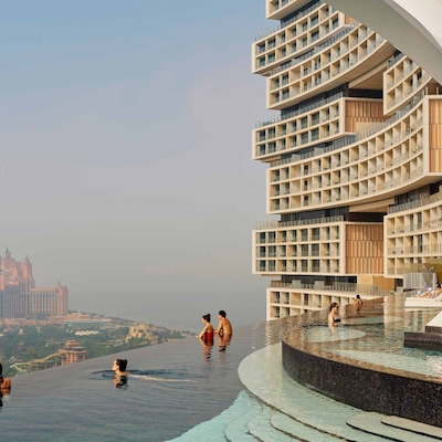 Des clients de l’Atlantis The Royal profitent de la piscine à débordement et de la vue sur Dubaï, mettant en valeur l’architecture moderne et incurvée du bâtiment de l’hôtel.