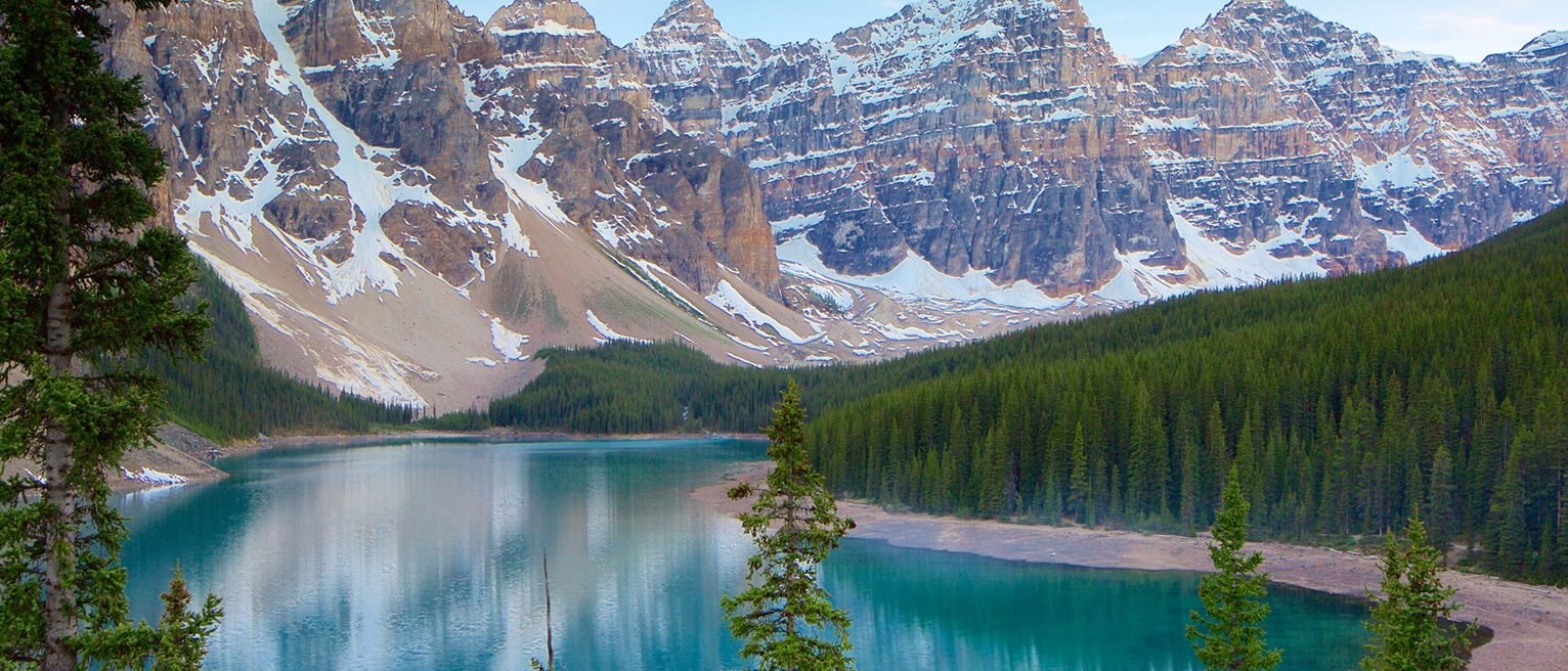 Turquoise Moraine Lake surrounded by dense evergreen forest and rugged snow-capped peaks in the Canadian Rockies.