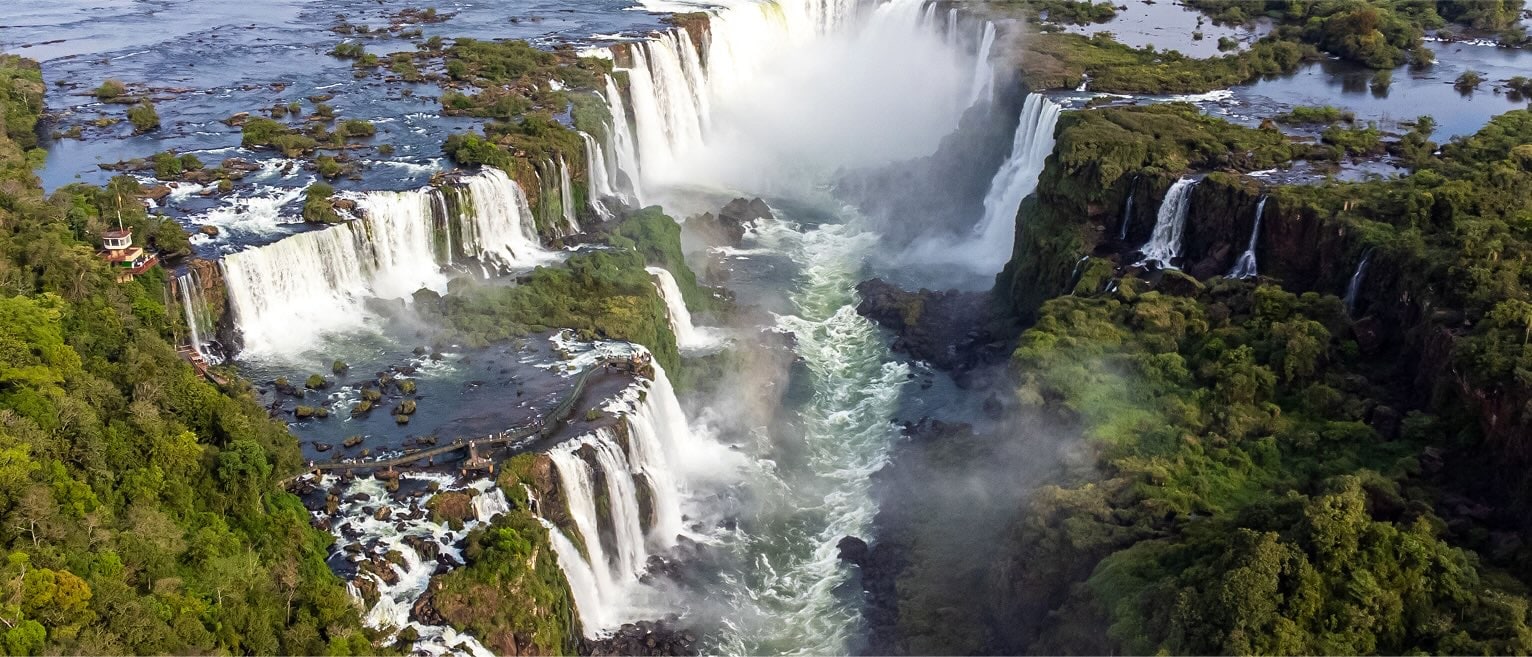 Aerial view of Iguazu Falls with multiple cascades thundering into the Iguazu River, surrounded by lush rainforest.