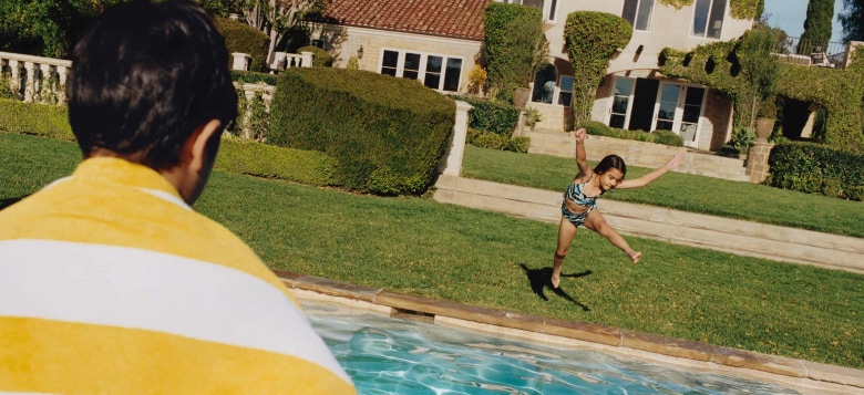 A girl appears mid-air, jumping into a pool, as a boy looks on