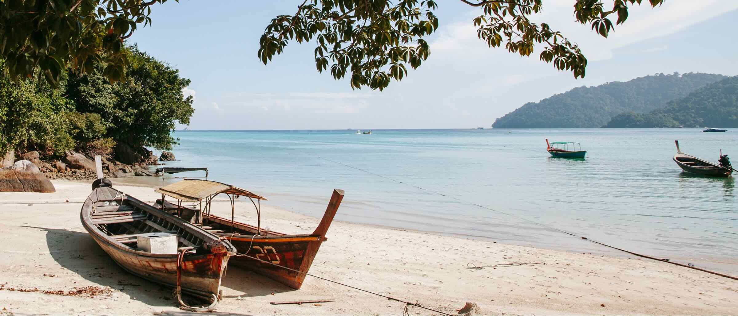 Two boats rest on the shore of a white sandy beach with views out onto the ocean.