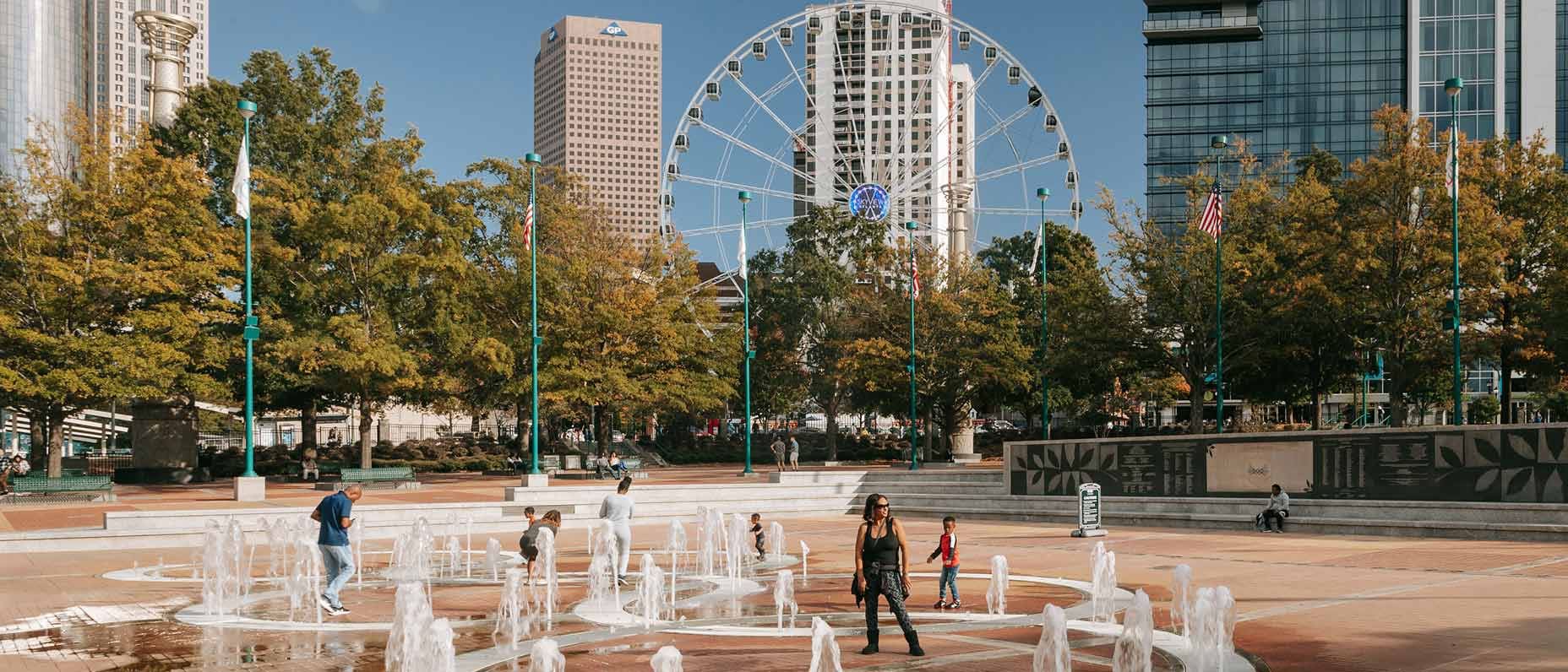 People walk through water fountains in a city square.