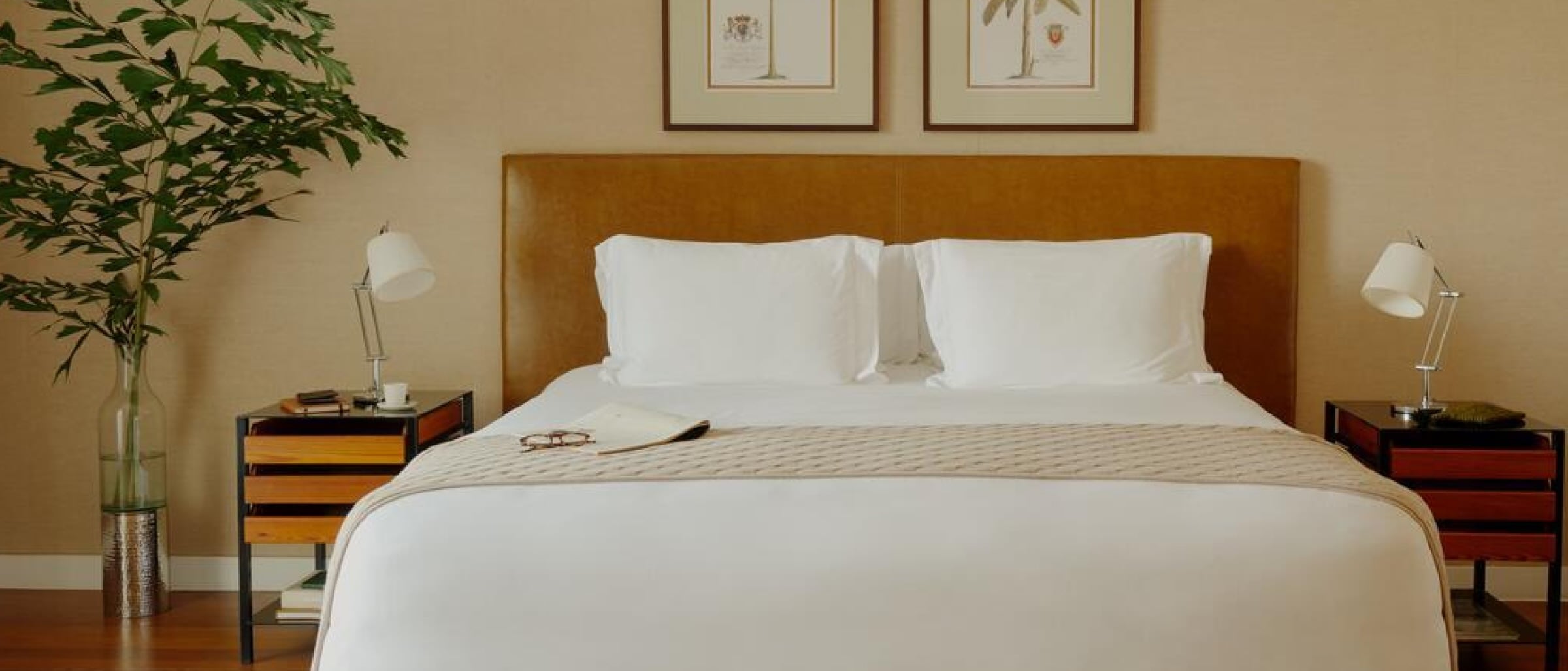 Uma cama de casal grande e moderna com lençóis brancos entre duas mesas de cabeceira com abajures brancos.