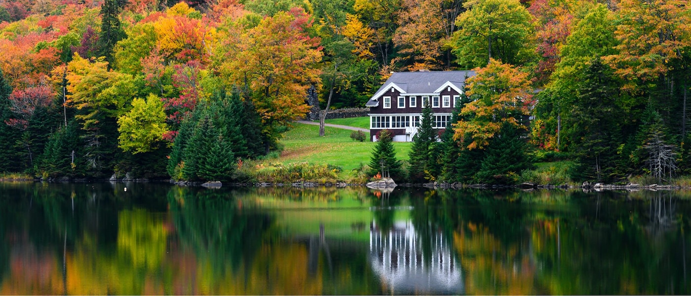 A traditional wooden-framed cabin on the edge of a large lake, surrounded by fall foliage.