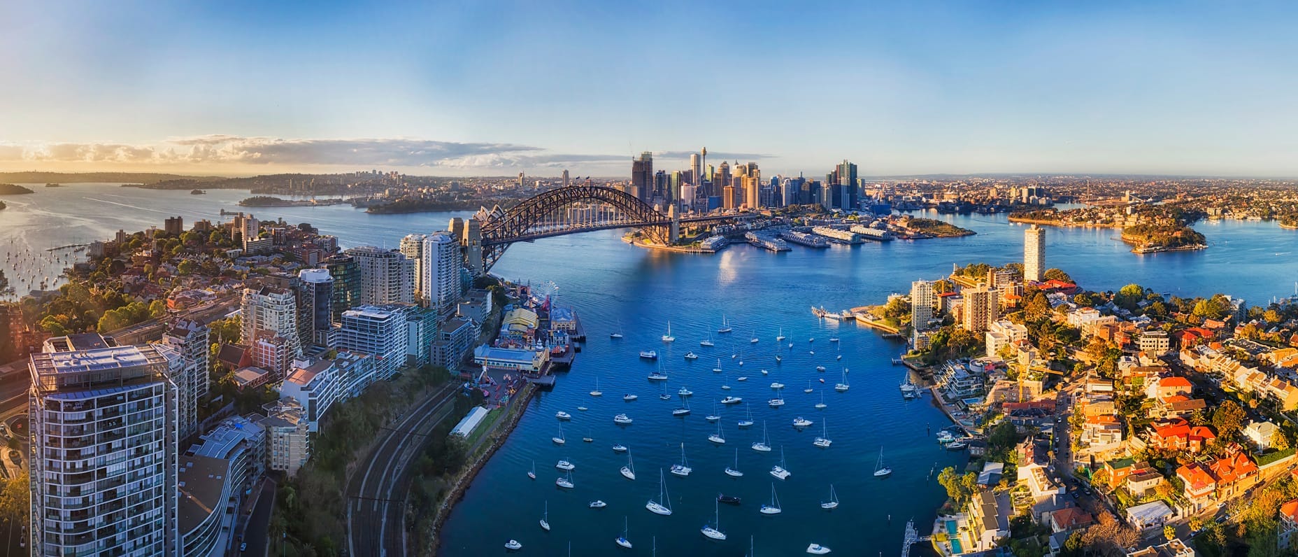 Coastal view of Sydney with the Harbour Bridge, Opera House and boats dotting the sparkling blue water on a sunny day.