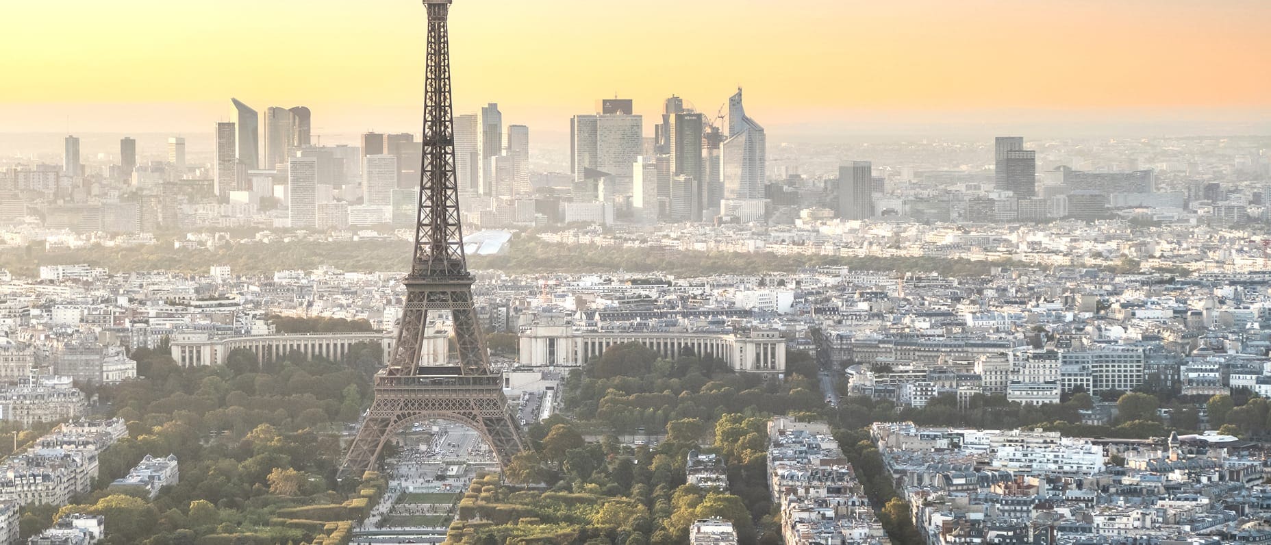 Panoramic view of Paris with the Eiffel Tower at the centre, bathed in golden light with the city stretching into the horizon.