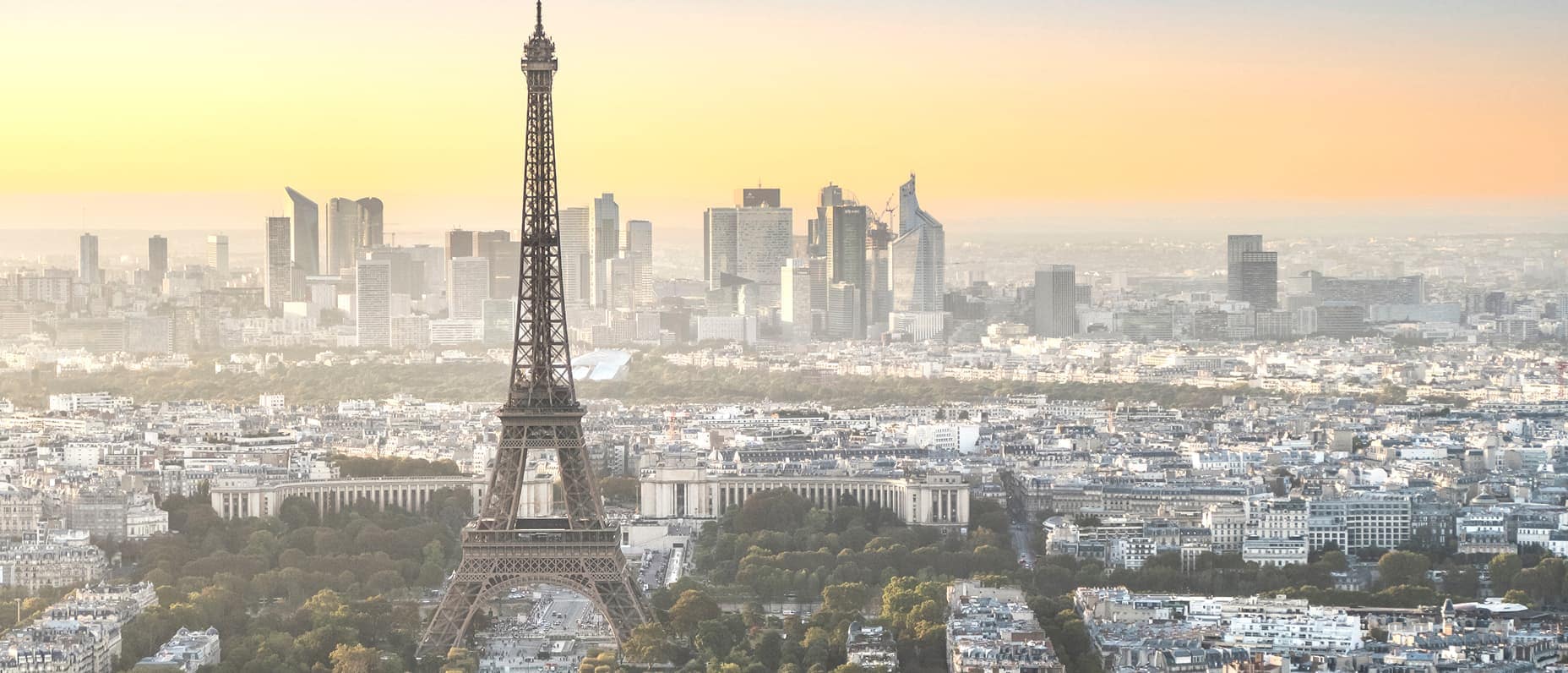 Vue panoramique de Paris avec la tour Eiffel au centre qui baigne dans une lumière dorée et la ville qui s’étend à l’horizon.