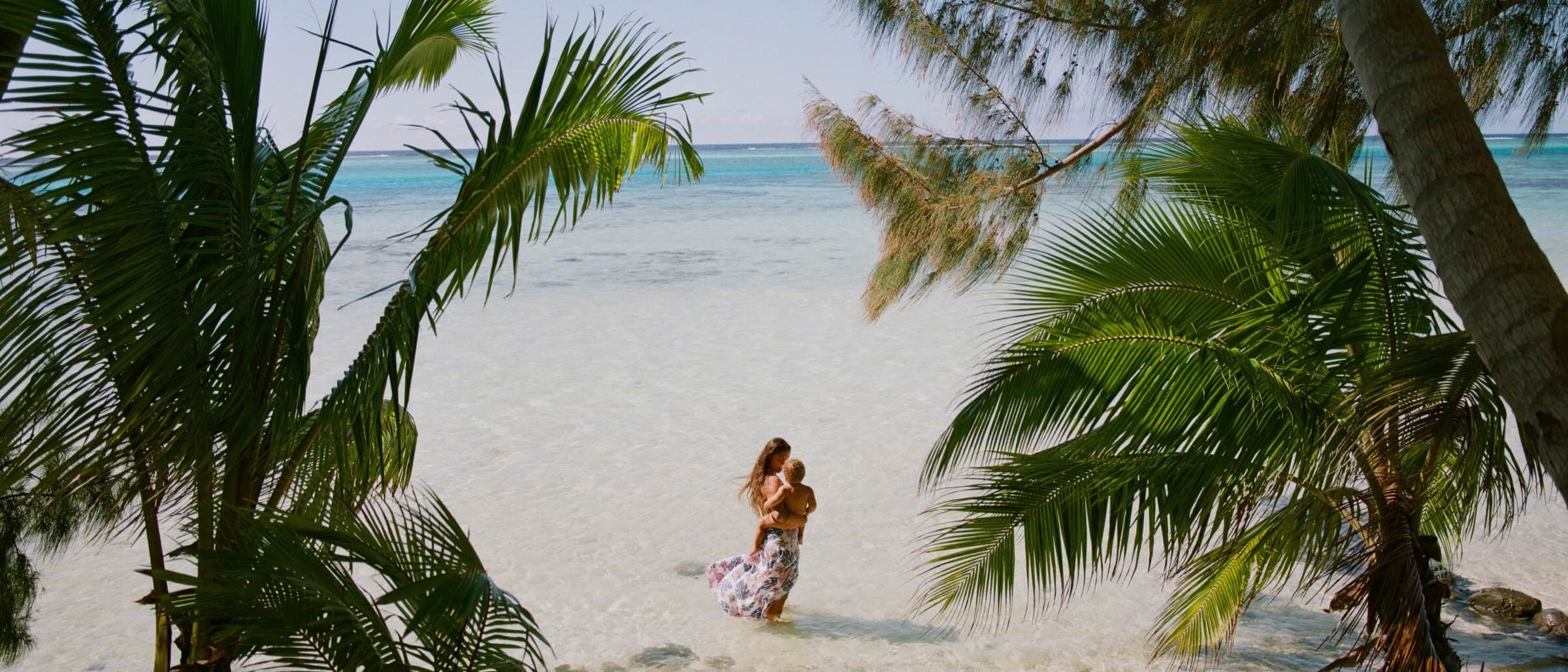 Person walking along a white sandy beach lined with palm trees.
