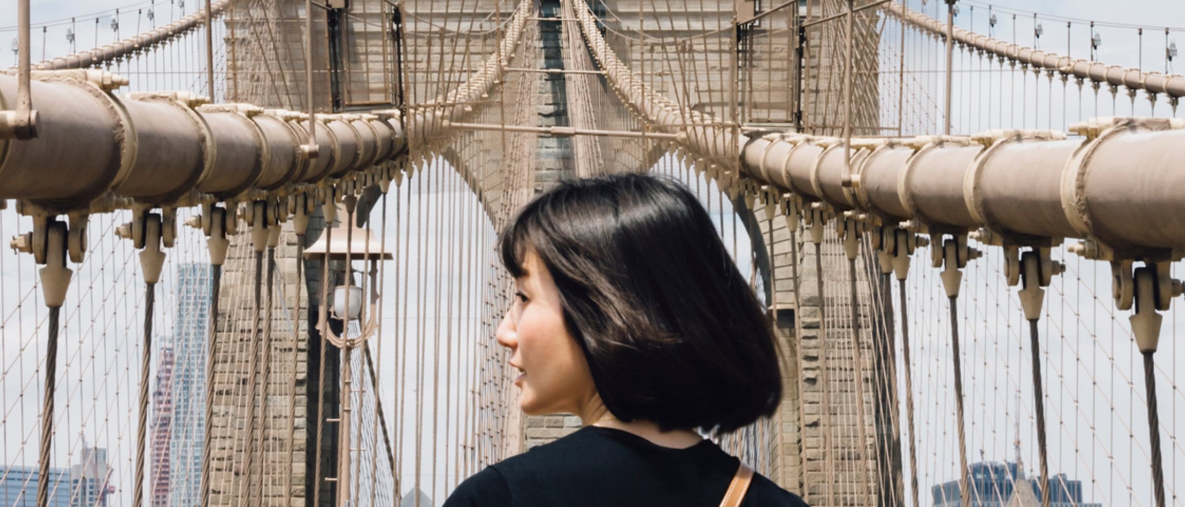 Back view of a person walking across the Brooklyn Bridge on a clear day.