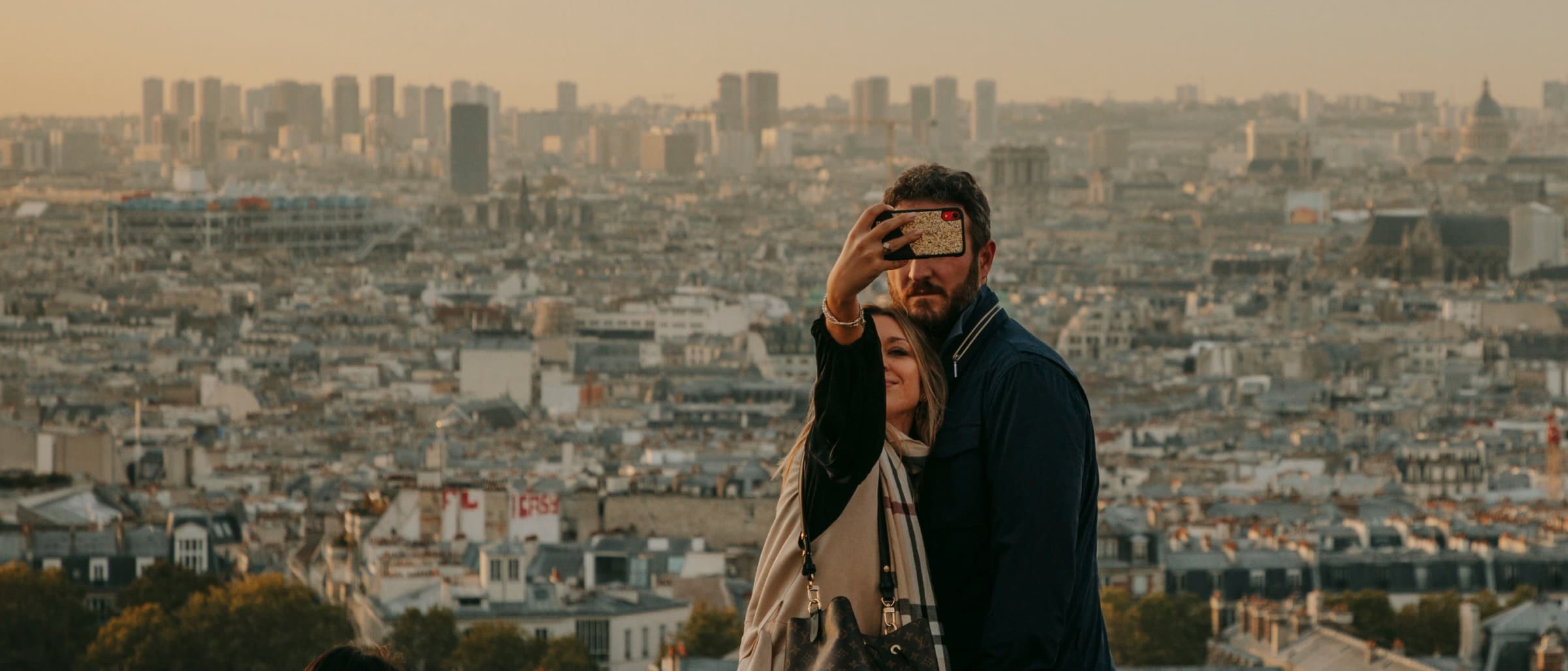 Couple embracing on a viewpoint overlooking a cityscape at dusk.