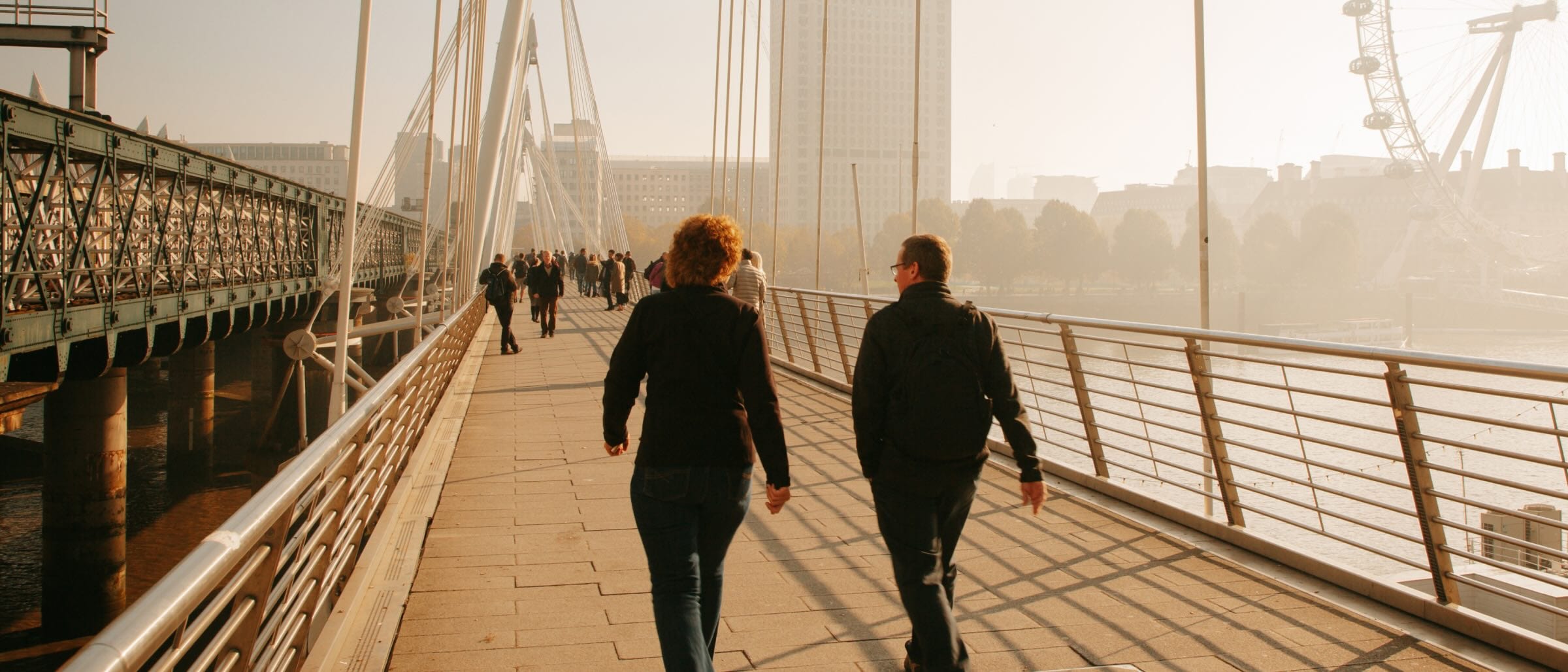 People walking across a bridge in London with the London Eye in the background.