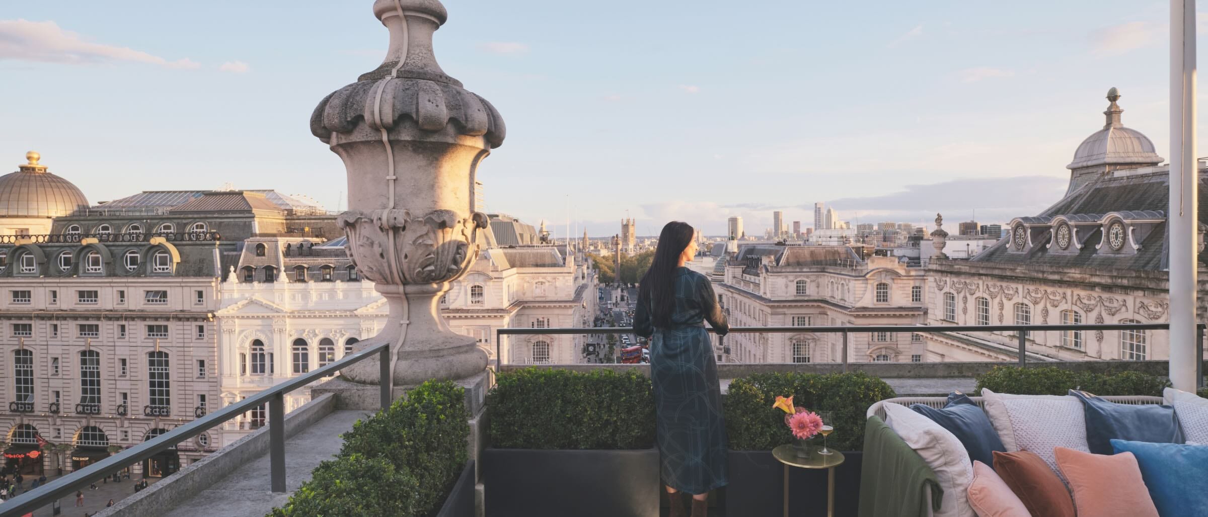A woman stands on a hotel rooftop looking out at the views of a picturesque city.