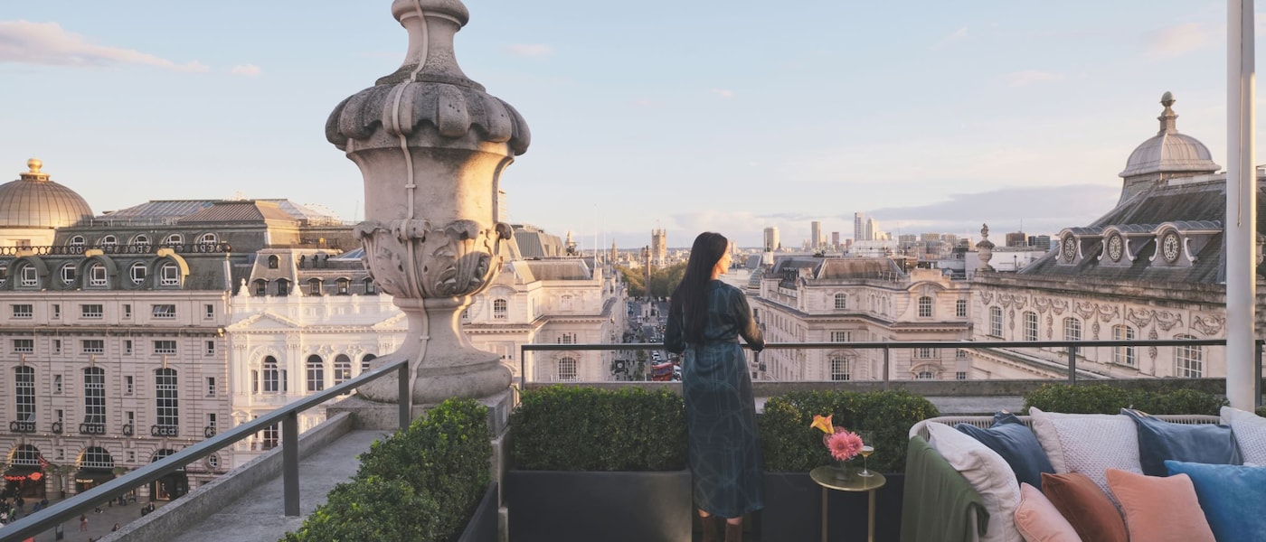 A woman stands on a hotel rooftop looking out at the views of a picturesque city. 