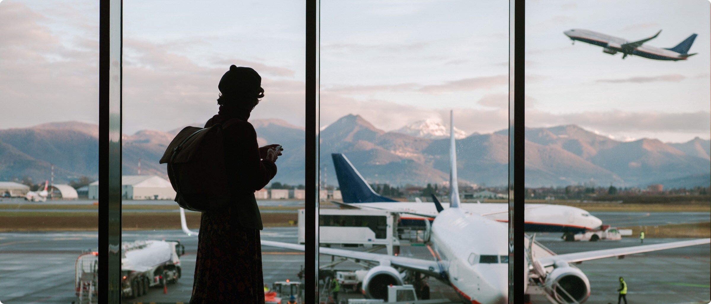 Ein Passagier blickt aus dem Flugzeugfenster in das sanfte Sonnenlicht. Es sind Wolken und blauer Himmel zu sehen.