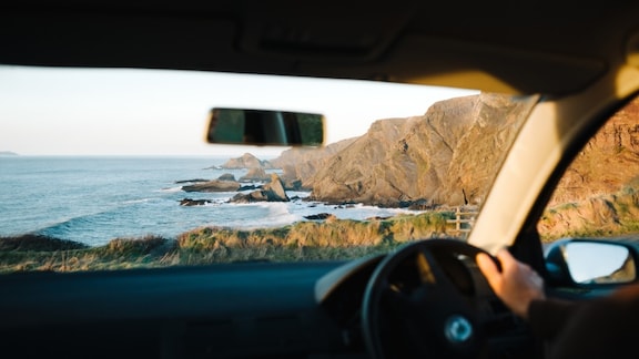 Una persona manejando mira las montañas que bordean la orilla del mar