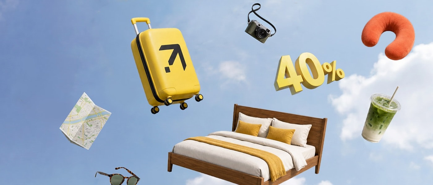 Una maleta amarilla con el logo de Expedia, una cama de hotel, un mapa, lentes de sol, una cámara, una almohada de viaje y una bebida con hielo flotan sobre un cielo azul claro, con un gráfico de un 40% en color amarillo llamativo en el centro.