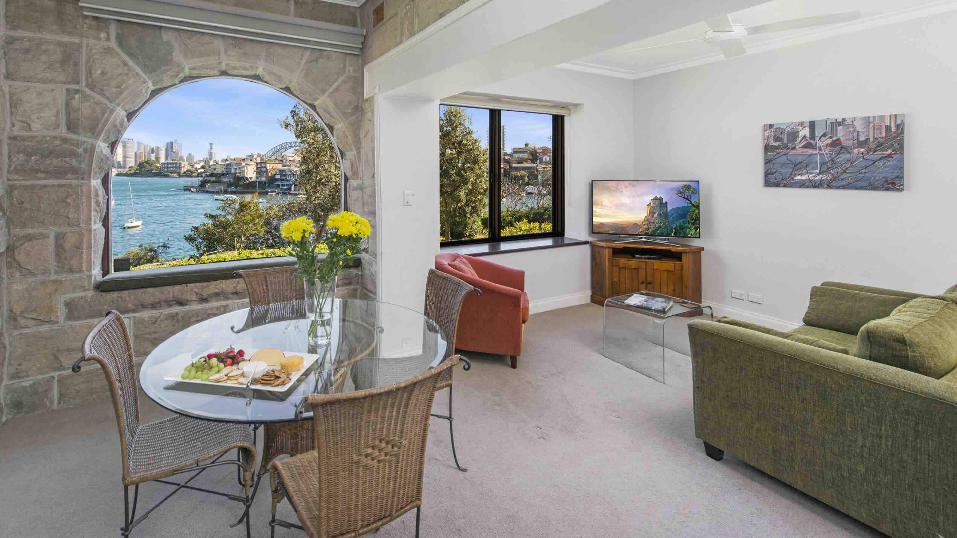 A living and dining space in a Sydney vacation rental, with stone walls in the dining area and a view from the window of Port Jackson and Sydney Harbour Bridge.  