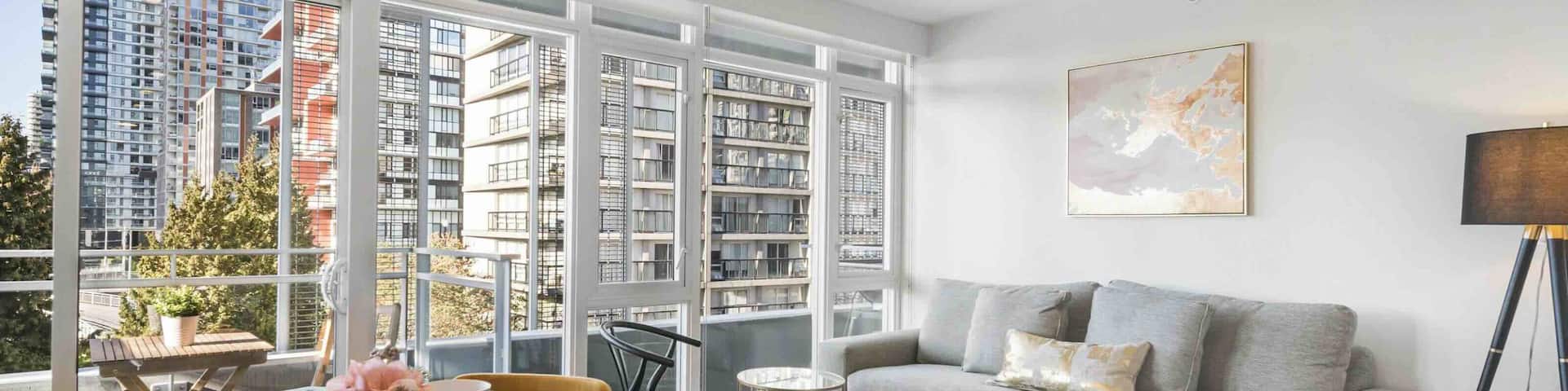 An open-plan living space in an apartment with a dining table and four mustard-coloured chairs, a grey sofa and a balcony with views of Ontario’s skyscrapers.