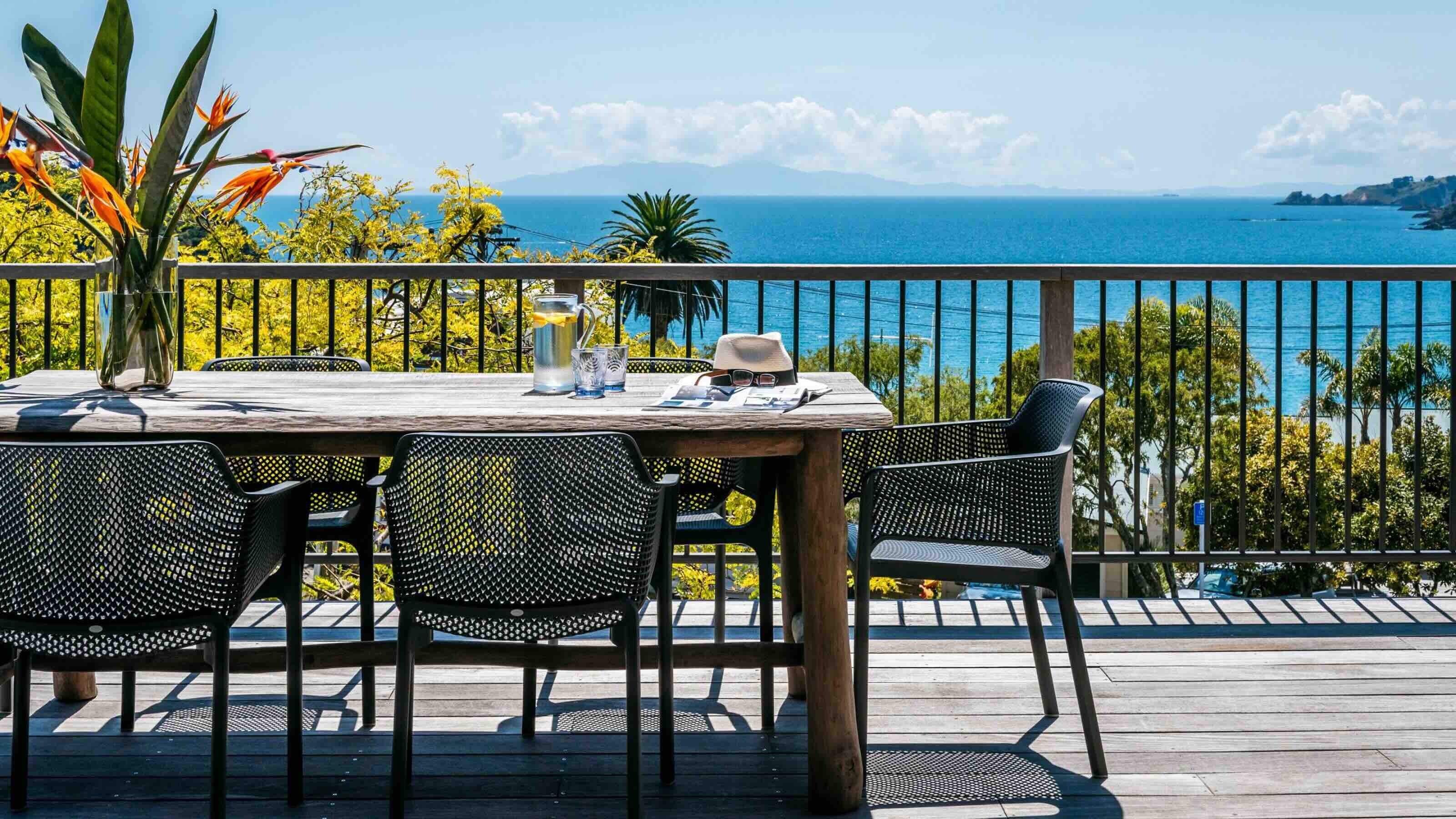 A view from the deck of a holiday apartment located on Waiheke Island, New Zealand. The deck features a six-seater table with views looking out onto Oneroa Bay. 