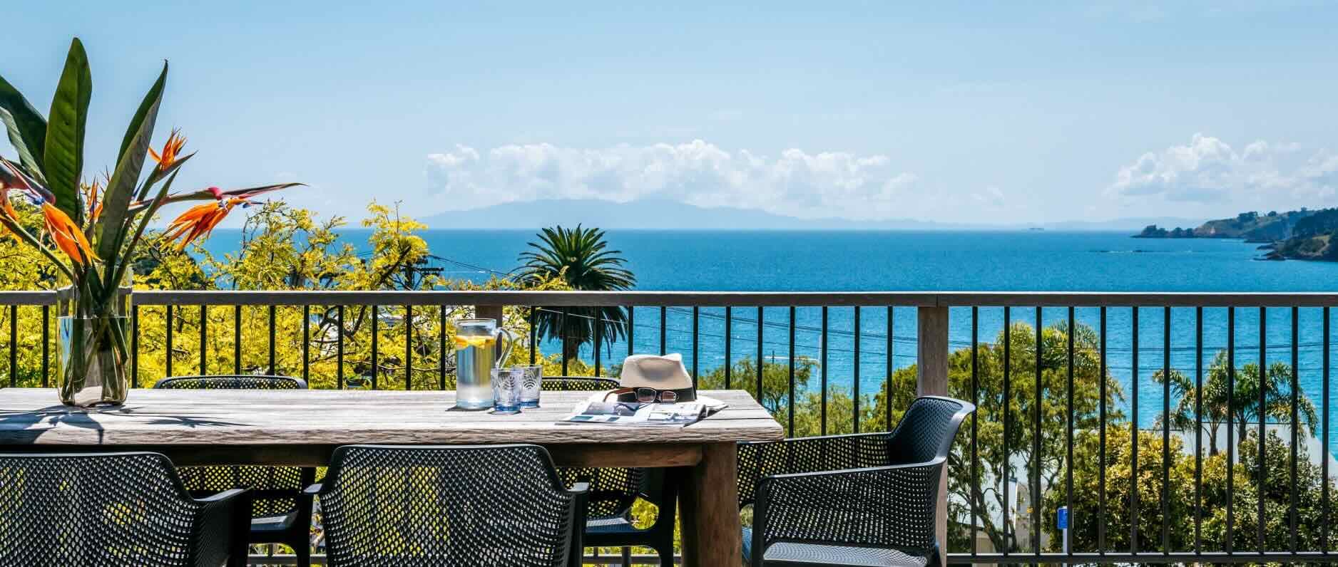 A view from the deck of a holiday apartment located on Waiheke Island, New Zealand. The deck features a six-seater table with views looking out onto Oneroa Bay. 