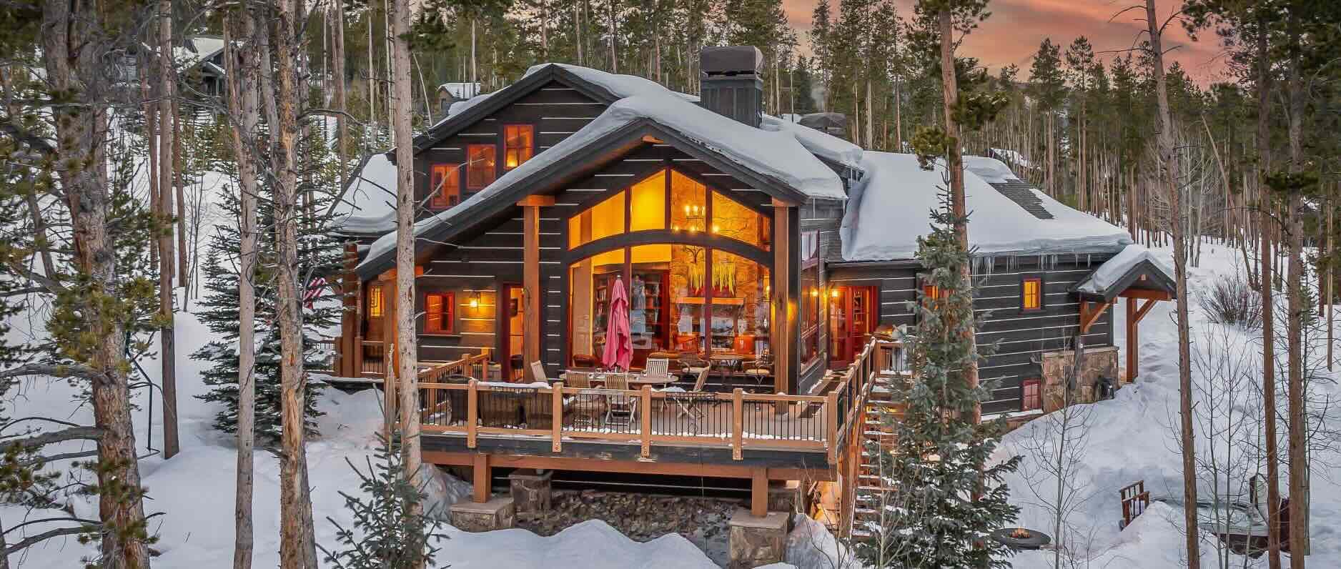 A luxury wooden ski chalet featuring an outdoor seating area and a view through a large window into the living space.  
