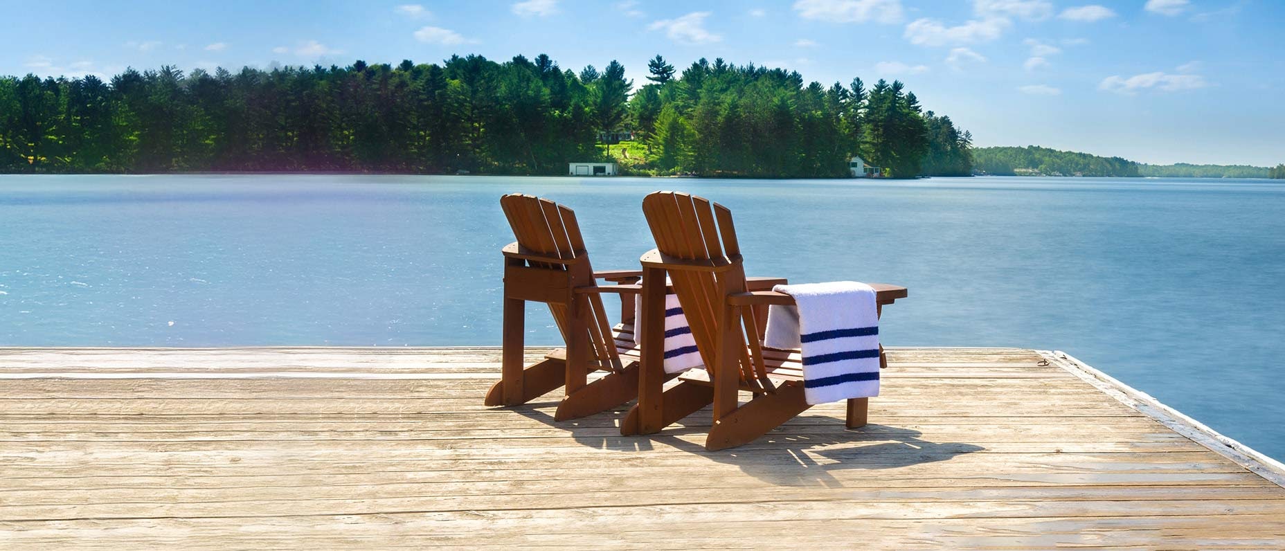 Two deck chairs look out over a lake surrounded by trees.