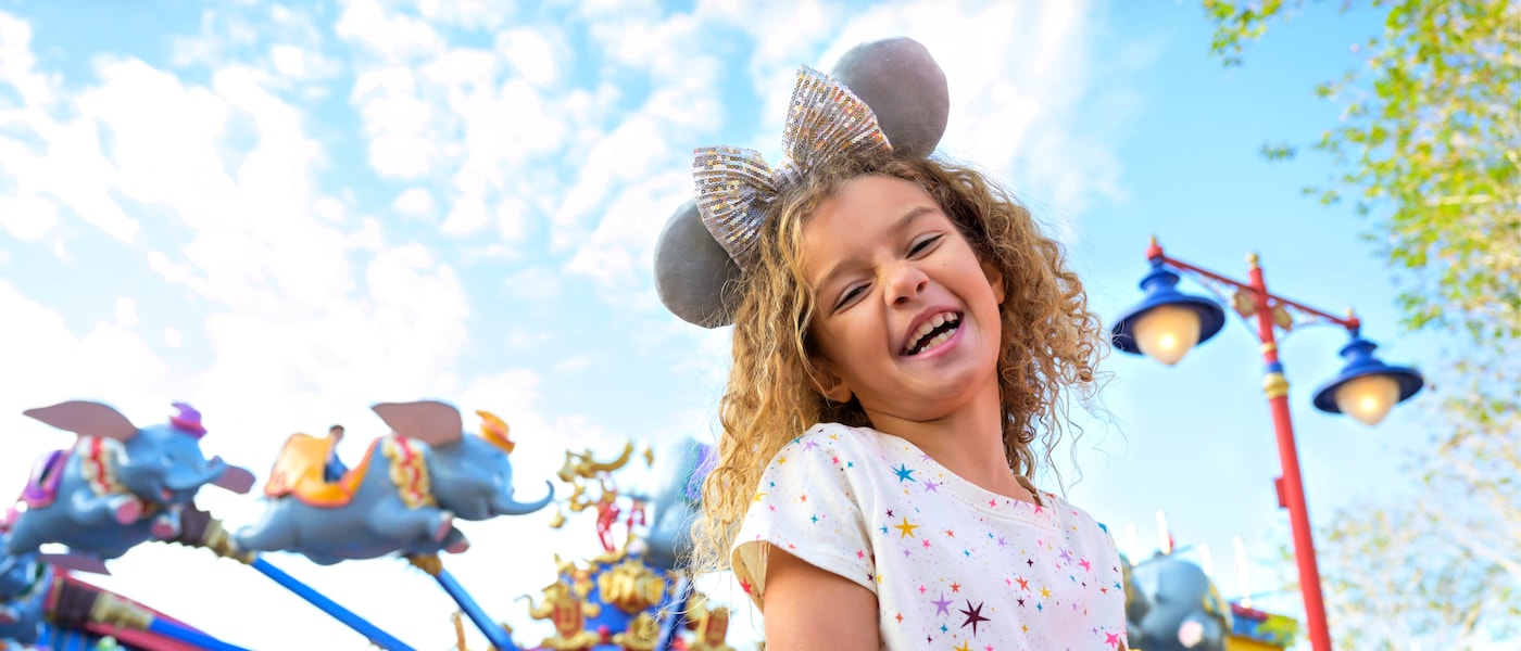 Niña usando orejas de ratón enfrente de un juego de un elefante volador.