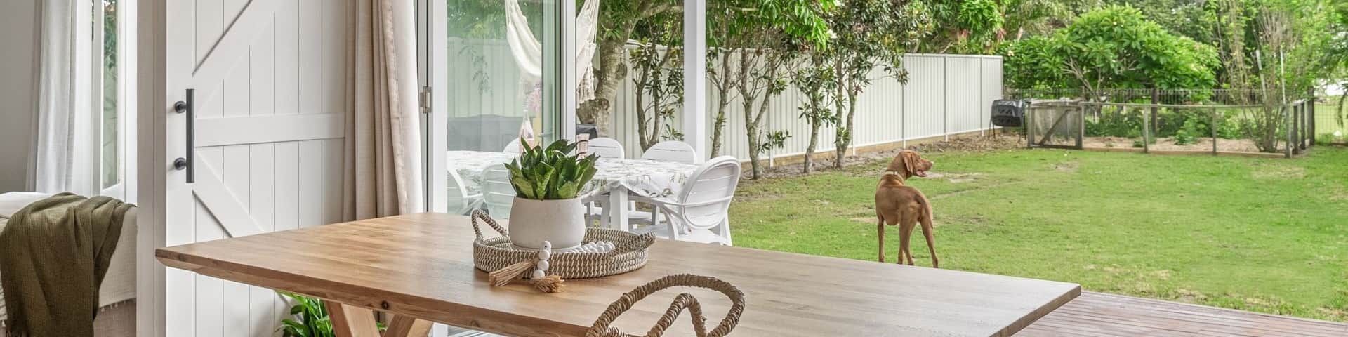 Un espace de vie sâouvre sur une terrasse et un jardin, oĂč joue un chien au pelage marron.