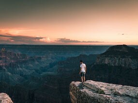A young man overlooking an inspiring view of an dark Grand Canyon in Arizona with an orange sky