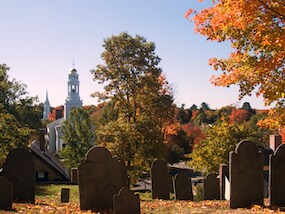 Tombstones in front of a church on a sunny fall day with green, orange, red and yellow foliage surrounding