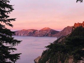 Scenic view of the sea with trees in the foreground and mountains in the background during a pink and orange sunset