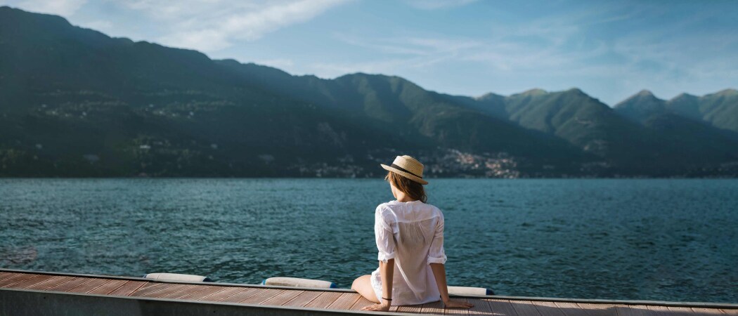 Una mujer se sienta en un muelle con vista al agua y las montañas.