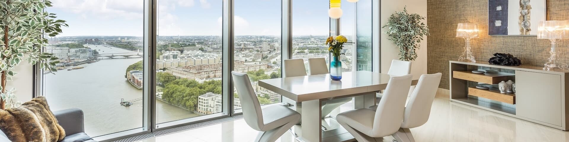 A dining room with modern furniture and floor-to-ceiling windows overlooks the River Thames in London