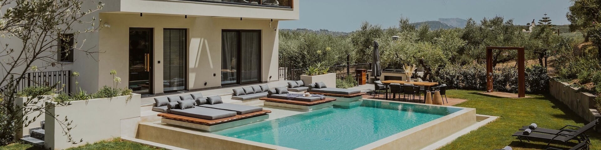Une maison à deux étages avec piscine privée. Dans le jardin verdoyant se trouvent des lits bain de soleil et un coin repas.