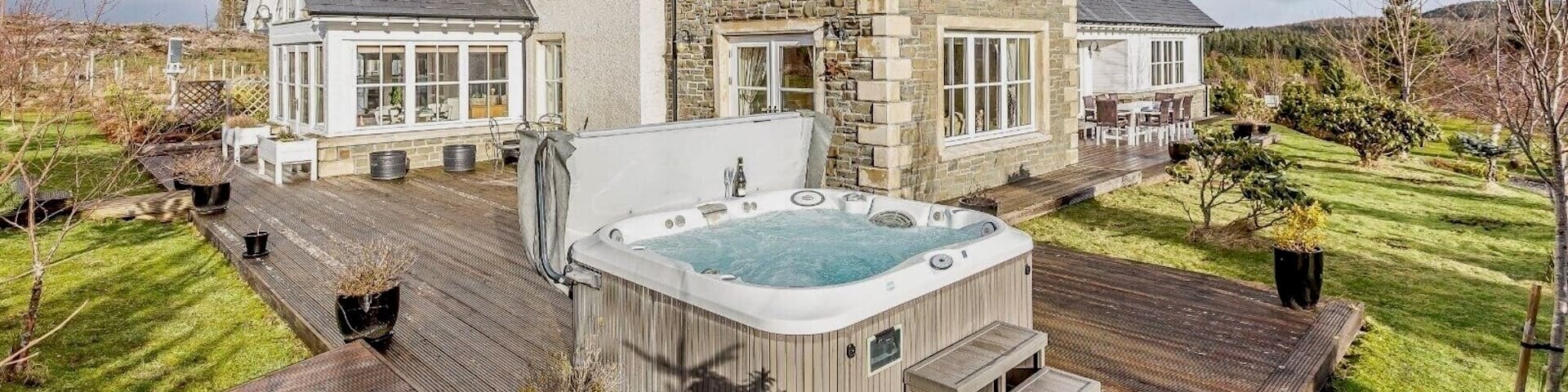 Bubbling hot tub sitting on a large wooden patio of a beautiful brick cottage.