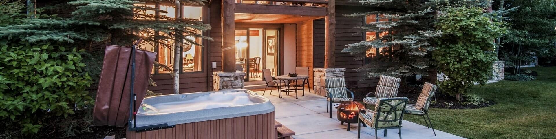 Une baignoire à remous bouillonnante, des tables et des chaises installées sur le patio énorme d’une propriété de vacances rustique vaste et magnifique.