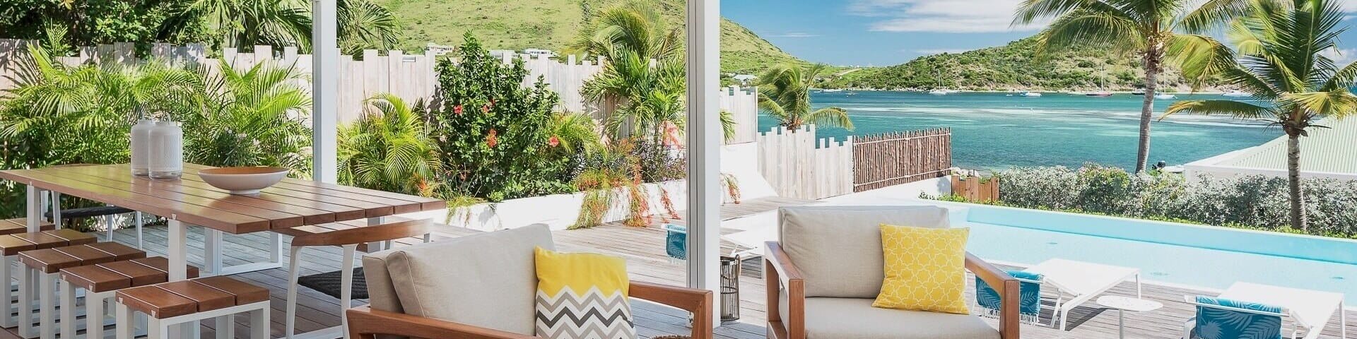 A patio with dining table offers views of the waterfront in a tropical location.