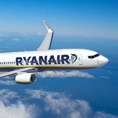 A Ryanair plane flying through a blue sky with scattered clouds.
