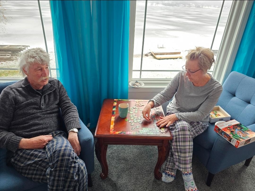 Siblings completing a jigsaw puzzle and having morning coffee while in their cozy pajamas.
