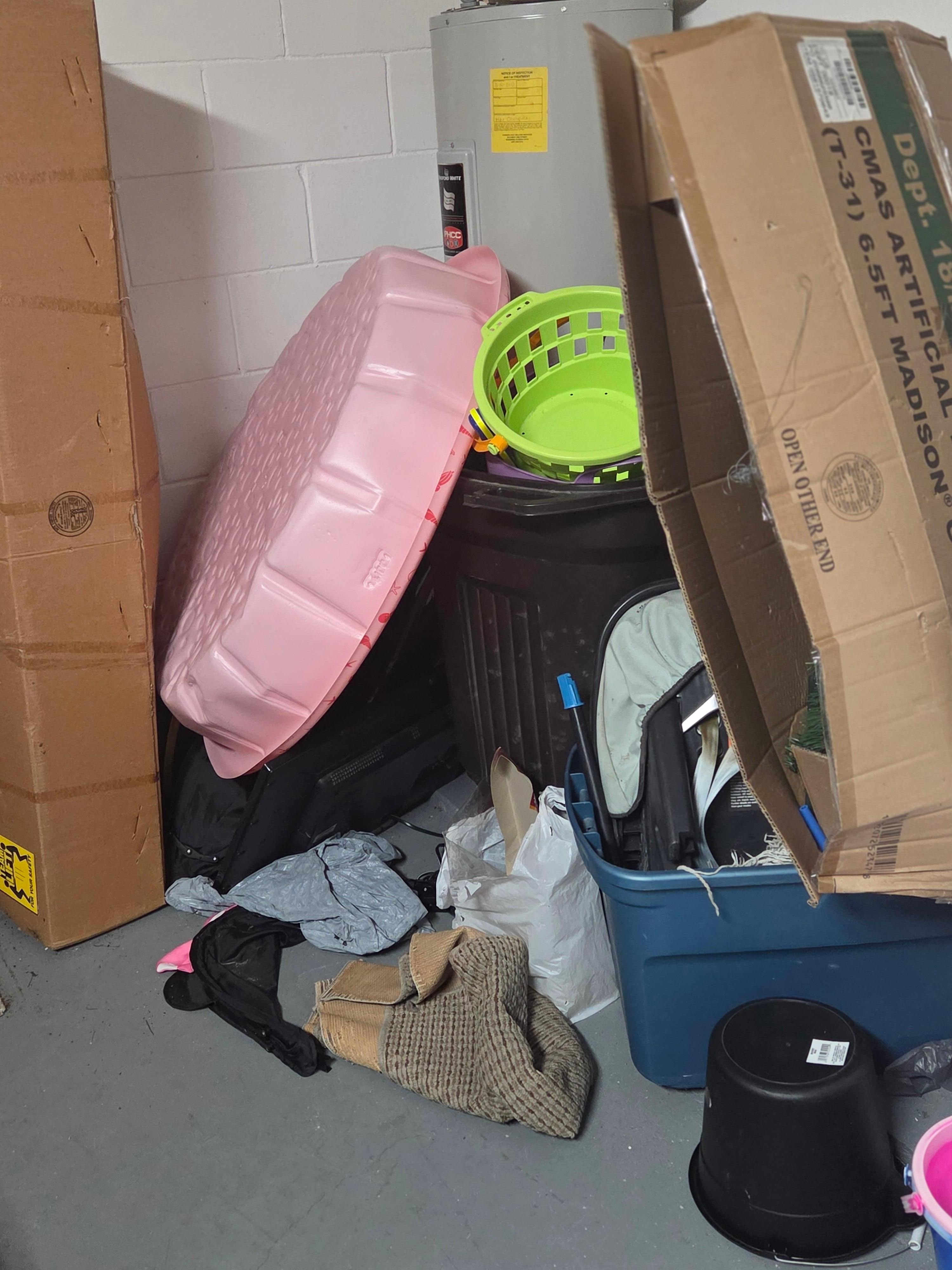 Junk piled up in the corner of the garage christmas trees, christmas ornaments, kitty pools, beach toys, garbage bags, linen bags