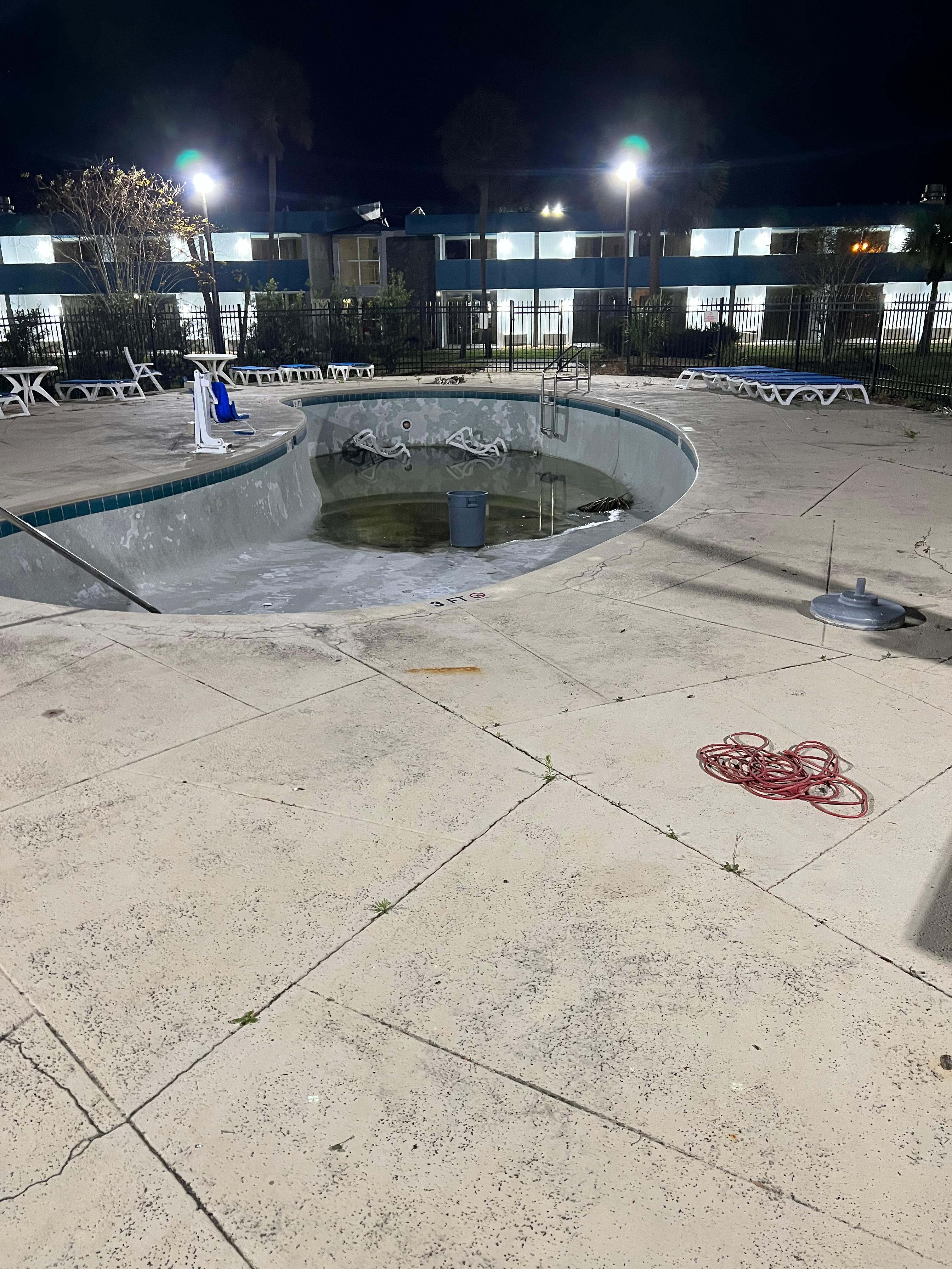 Pool with trash can and chairs but very little water. 