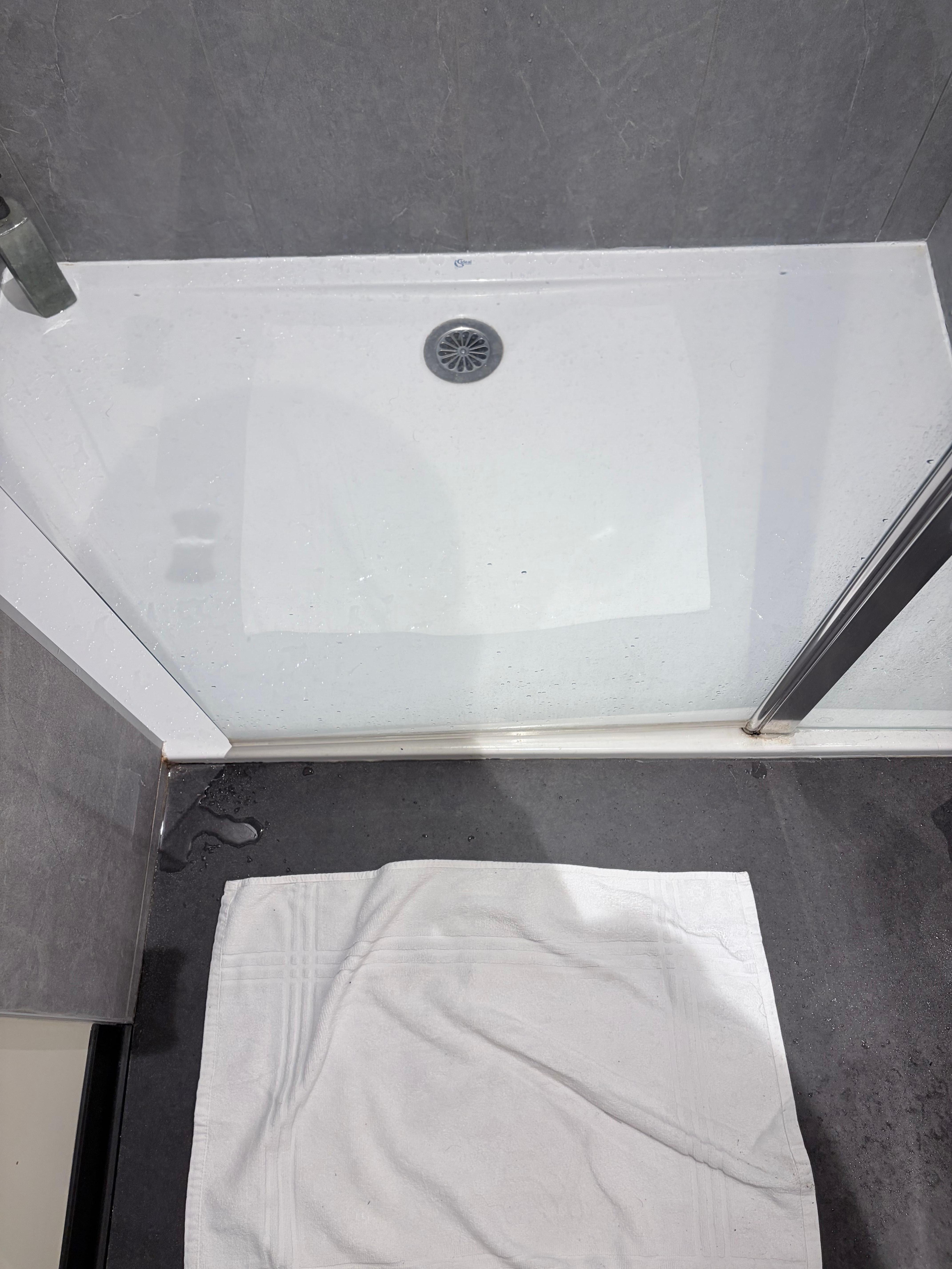 Porte de douche trop courte. L’eau passe entre le mur et la porte. Cela inonde le sol de la salle de bain