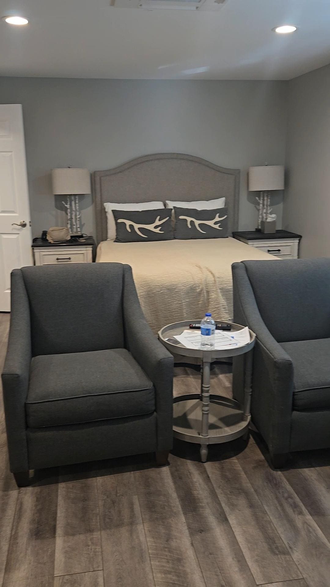 Bathroom to the left, full-size bed, two chairs, small table. Big screen tv mounted on the wall to the right above a fireplace.