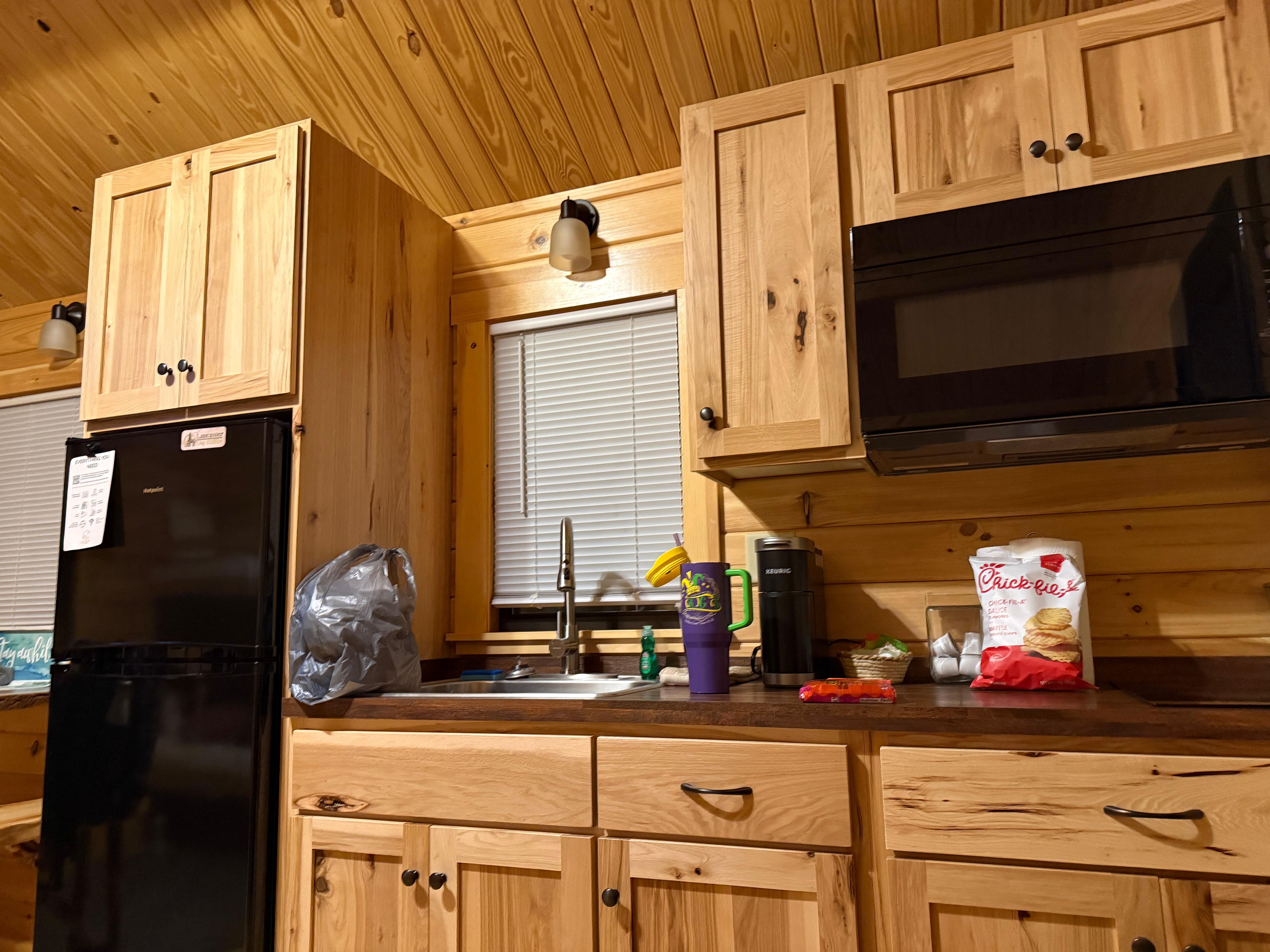 Apartment sized fridge, two burner stove, microwave, and toaster oven below. Basic cookware also present. 