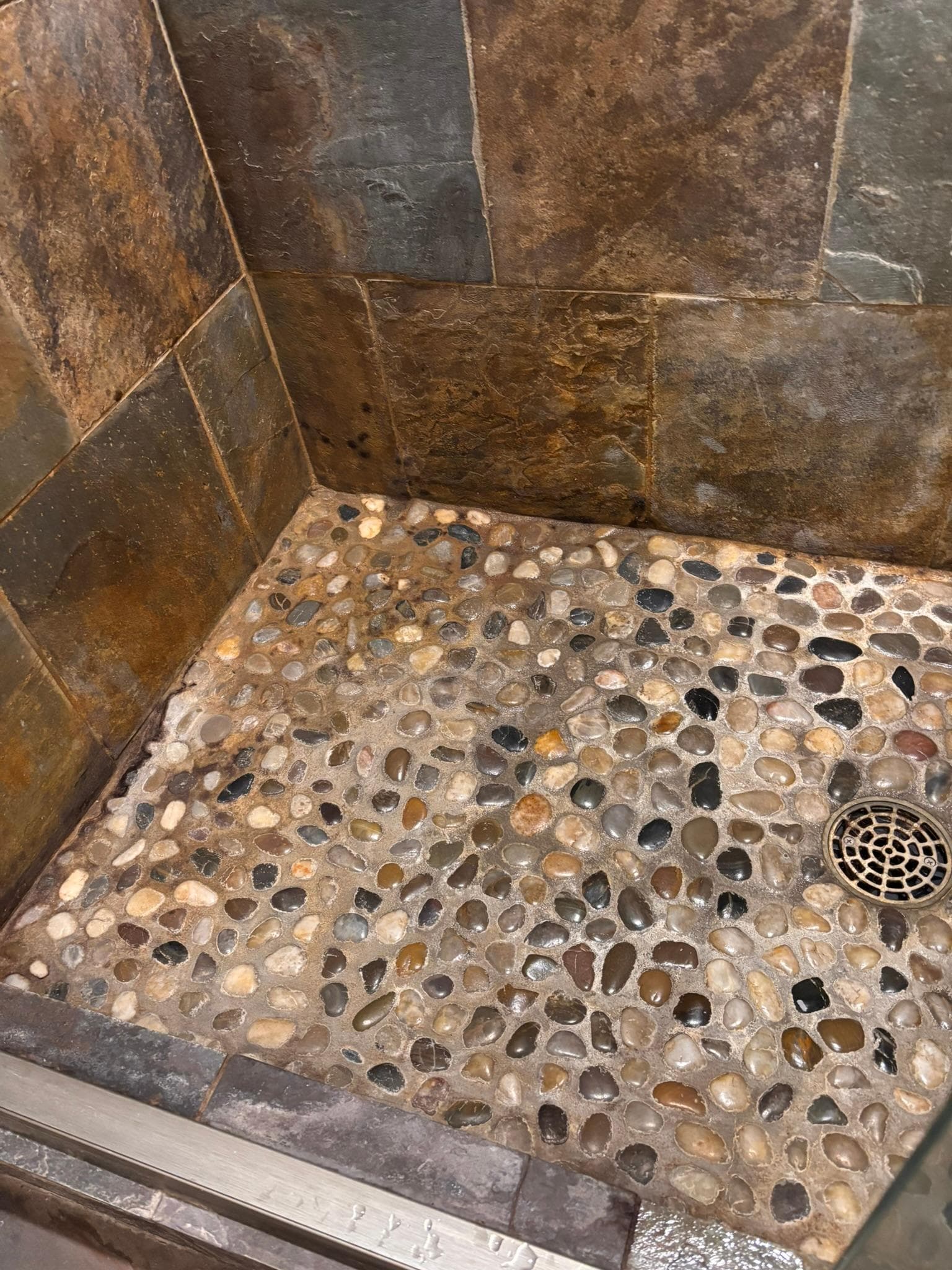 Dirty/moldy shower floor  made of uncomfortable river rocks.