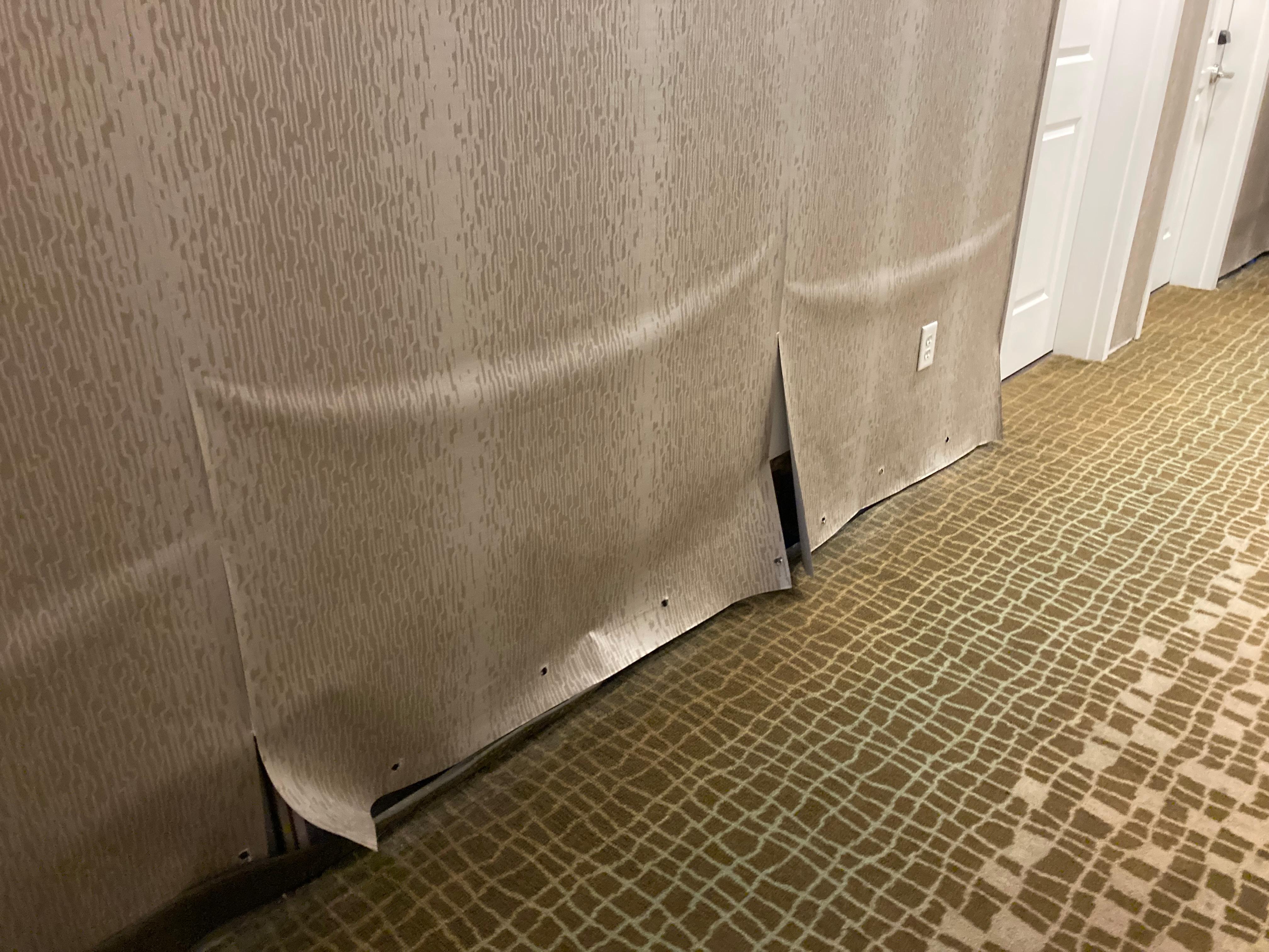 Water damage with drywall removed under and wall paper hanging to cover gaps