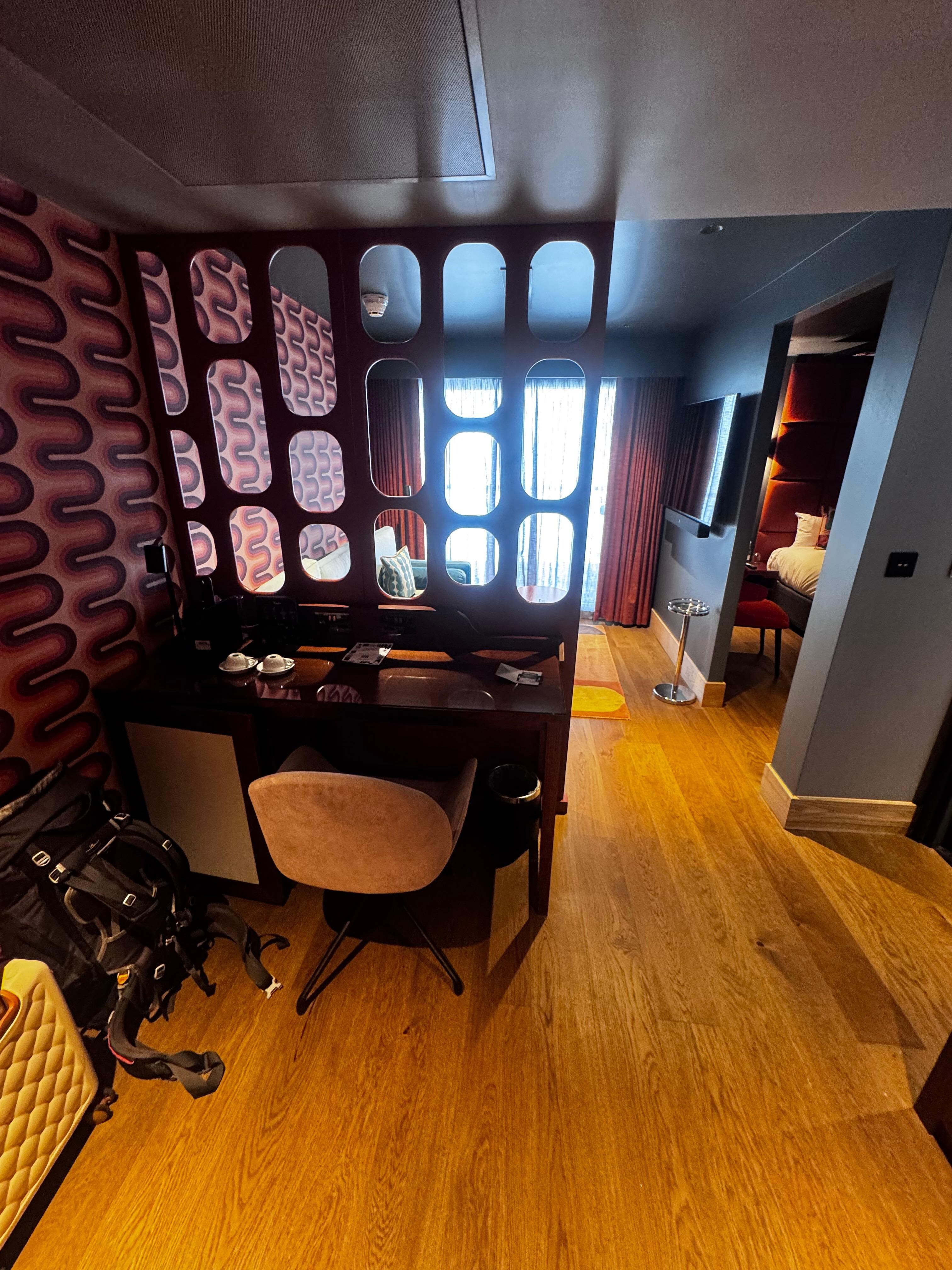 Desk and chair with fridge and safe in cupboard to left and coffee machine.