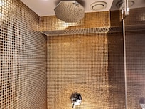 Banheiro com azulejo dourado, chuveiro grande e com alto fluxo de água