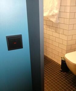 Bathroom light switch to left of wooden slat.